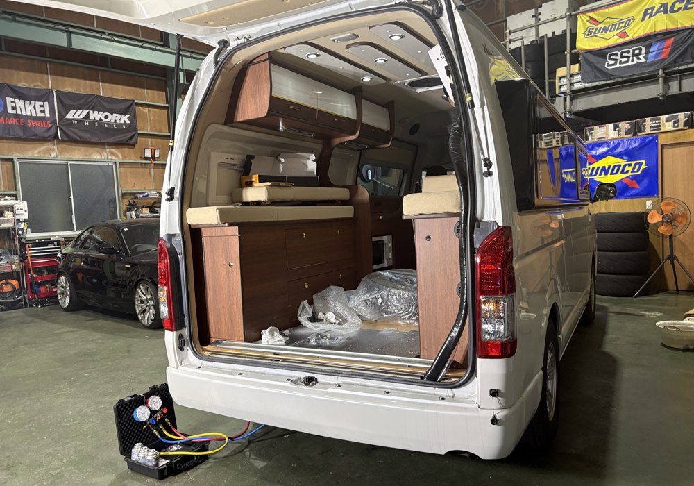 冷媒ガスの充填作業。車両後方でゲージ・ガス缶を使用